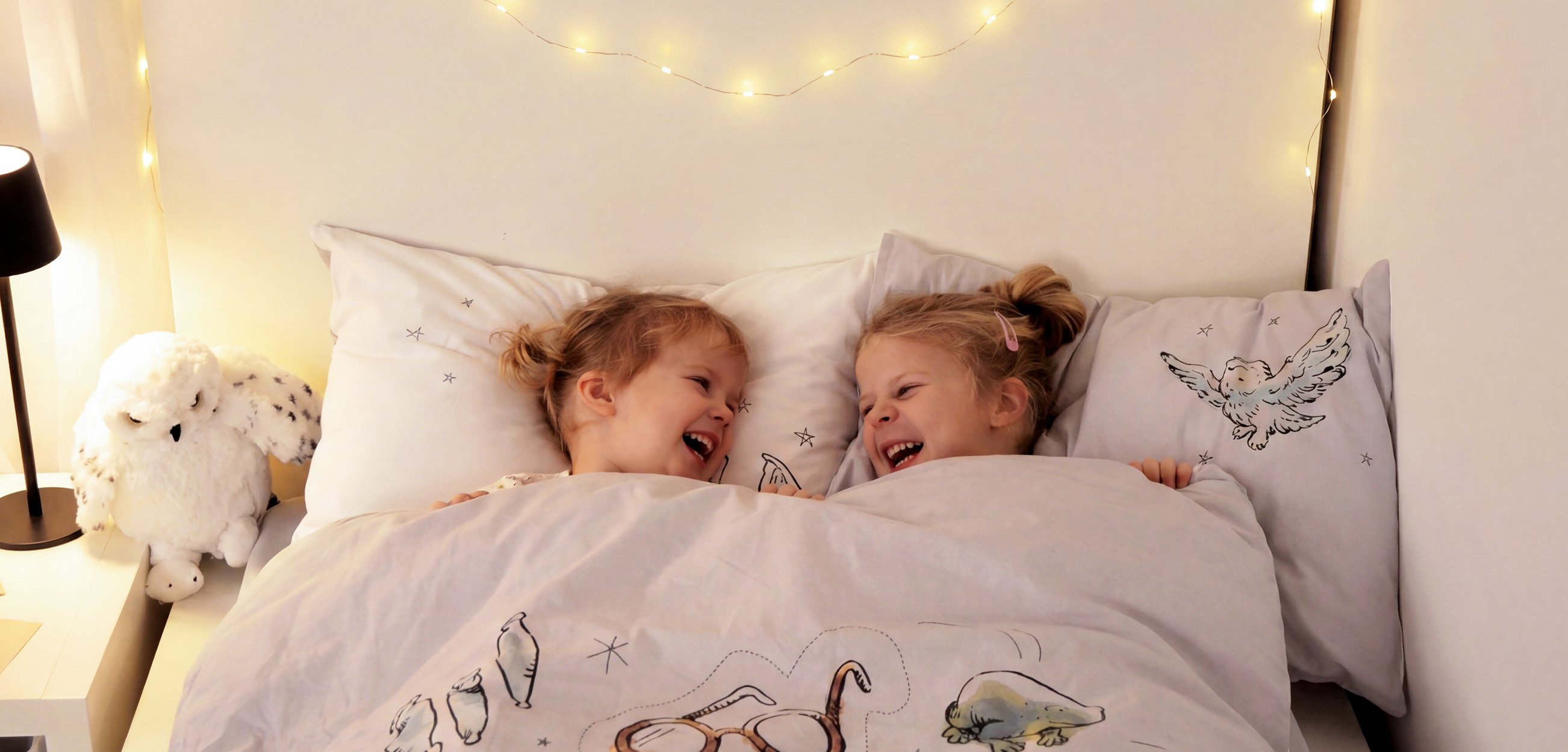 Zwei Kinder liegen glücklich in Babybettwäsche.