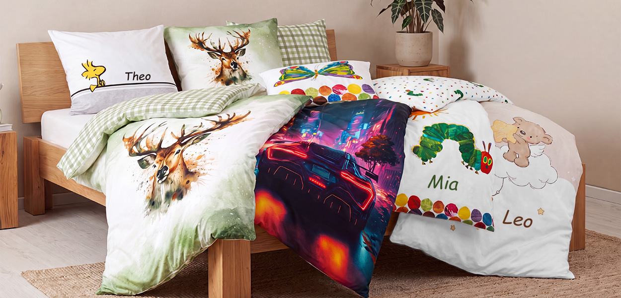 Das Bild zeigt verschiedene personalisierte Bettwäsche-Designs auf einem Kinderbett. Zu sehen sind unter anderem:- **Snoopy/Woodstock** mit dem Namen „Theo“
- **Hirschmotiv** in Aquarell-Optik
- **Bunter Schmetterling**
- **Neon-Sportwagen** im futuristischen Stil
- **Die kleine Raupe Nimmersatt** mit dem Namen „Mia“
- **Schutzengel-/Bärenmotiv** mit dem Namen „Leo“Die Motive reichen von kindlich-verspielt bis hin zu modern und auffällig und zeigen, dass sich Namen individuell aufdrucken lassen.