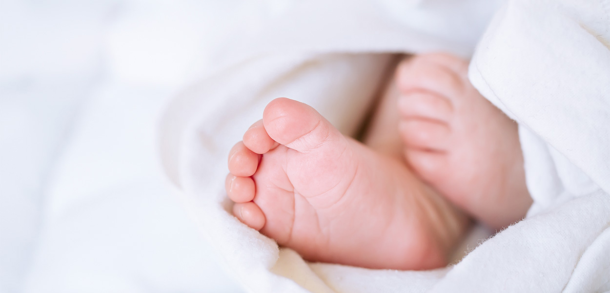 **Babydecke Größe**
Nahaufnahme von kleinen Babyfüßen, die unter einer weichen weißen Decke hervorschauen.