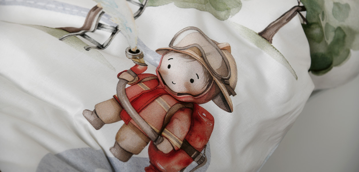 Kinderbettwäsche mit liebevollem Feuerwehr-Motiv: Auf weißem Stoff ist eine niedliche Figur in roter Einsatzkleidung zu sehen. Sanfte Grün- und Naturtöne sowie das dezente Pflanzenmotiv schaffen eine ruhige, kindgerechte Atmosphäre.