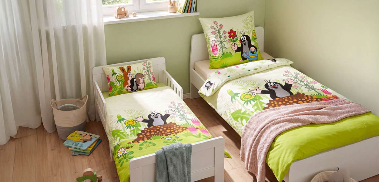 Kinderbettwäsche mit fröhlichem Maulwurf-Motiv in einer bunten Blumenwiese. Das Bild zeigt die Bettwäsche auf zwei unterschiedlich großen Kinderbetten – ideal, um die Wirkung des Designs in verschiedenen Bettgrößen zu vergleichen. Die Farben in Weiß, Grün, Gelb und Rosa wirken freundlich und passen gut in ein helles Kinderzimmer.