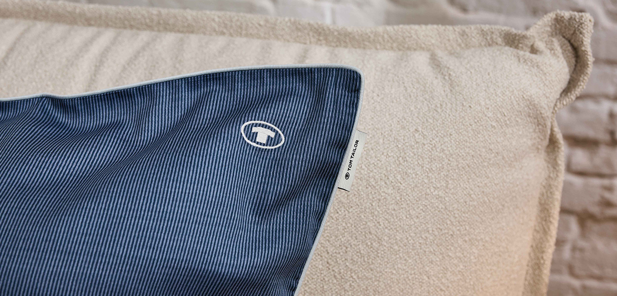 Sommerbettwäsche in dunkelblauem Nadelstreifen-Design mit hochwertigem Tom-Tailor-Label – stilvoll kombiniert mit einem weich strukturierten Kissen in Naturweiß.