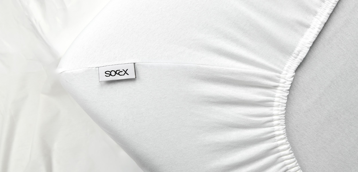 Weißes Spannbettlaken mit elastischem Rundumgummi und SOCKX-Label auf einer Matratze.