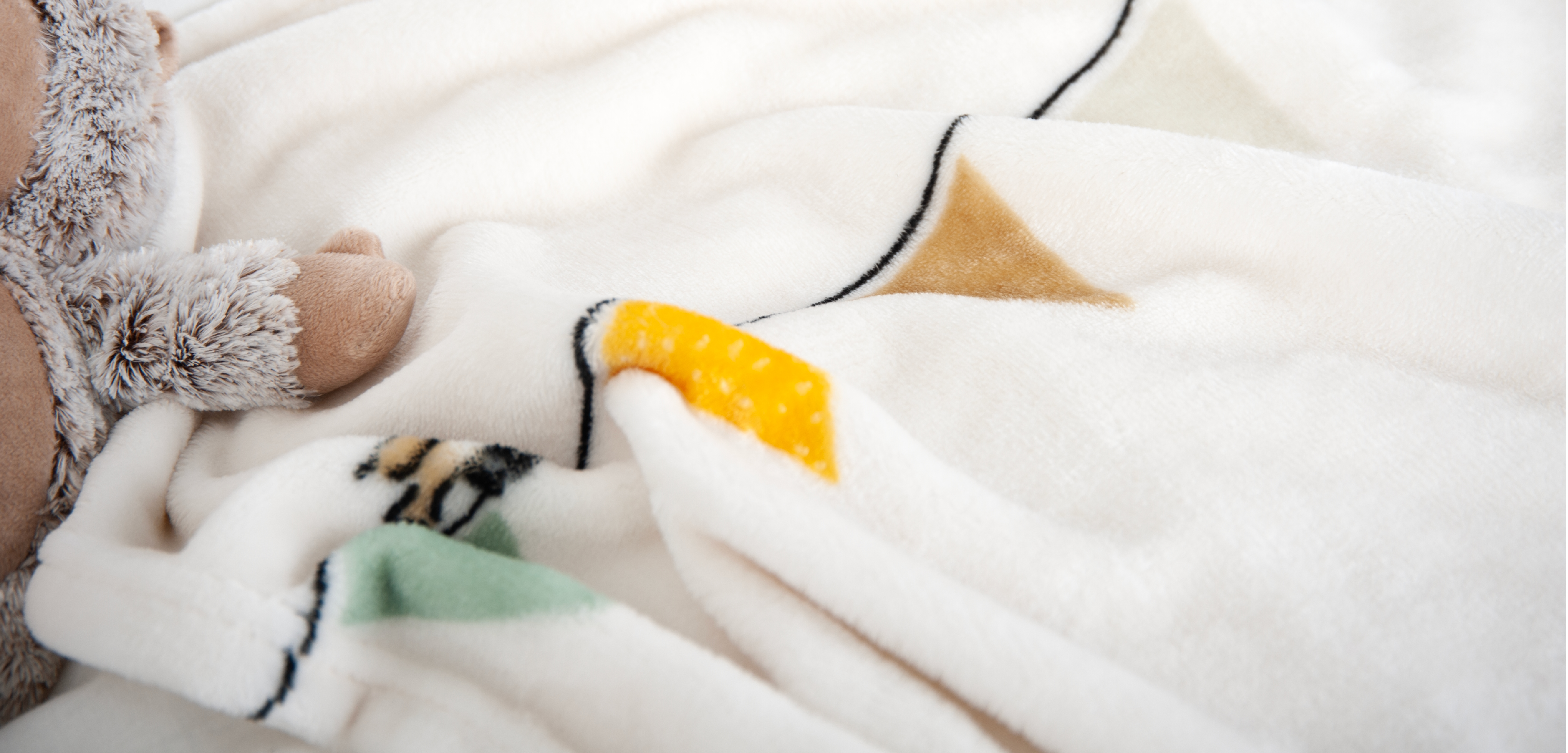Nahaufnahme einer besonders weichen, flauschigen Kinder-Kuscheldecke. Das helle Design zeigt freundliche Tiermotive in Grau, Gelb und Grün und vermittelt Wärme, Komfort und Geborgenheit.
