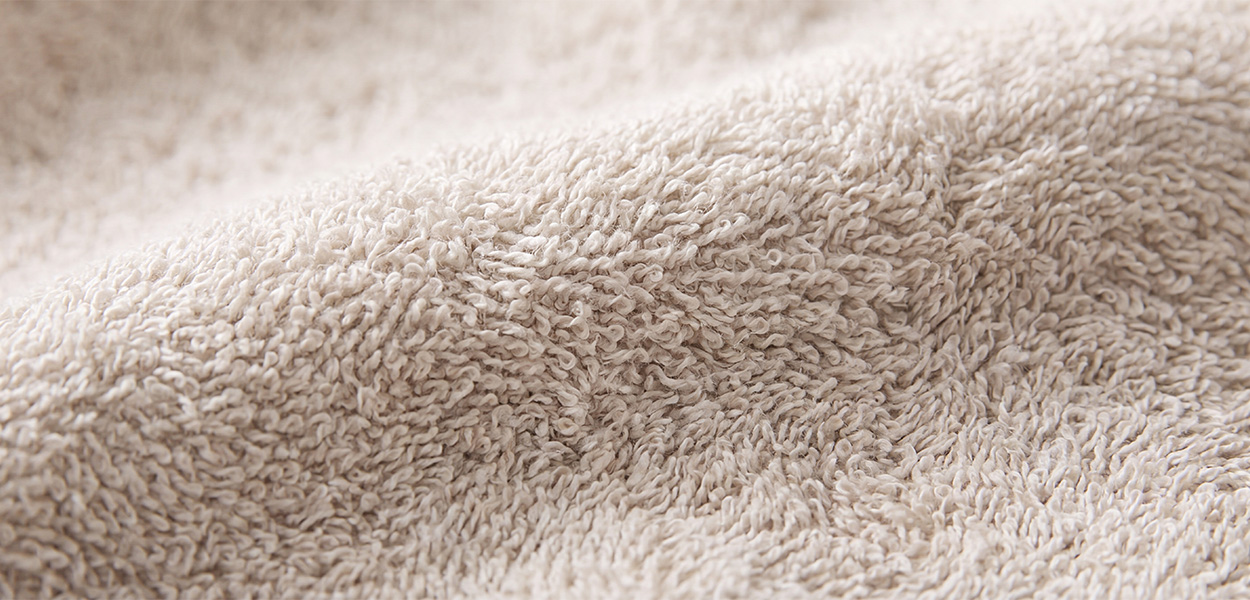 Das Bild zeigt eine Nahaufnahme eines beigefarbenen Duschtuchs. Das Material wirkt weich, flauschig und saugfähig, mit dichter Schlingenstruktur wie bei Frottee.