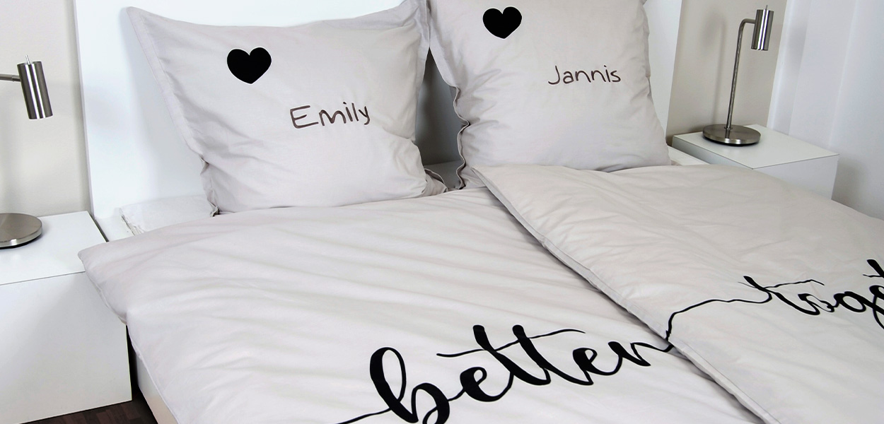 Weiße personalisierte Bettwäsche mit den Namen „Emily“ und „Jannis“, schwarzen Herzen und dem Schriftzug „better together“.